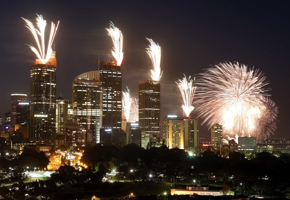 Image: Fireworks explode on the rooftops of buildings during a show prior to the new year celebrations in Sydney